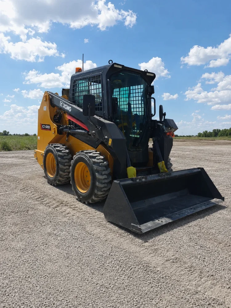 Компактен мини челен товарач XCMG XC7-SR08 в предно-десен изглед с кофа върху чакълен терен.